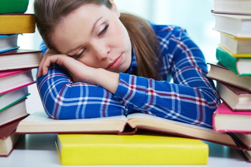 Pavargęs studentas miega ant vadovėlių