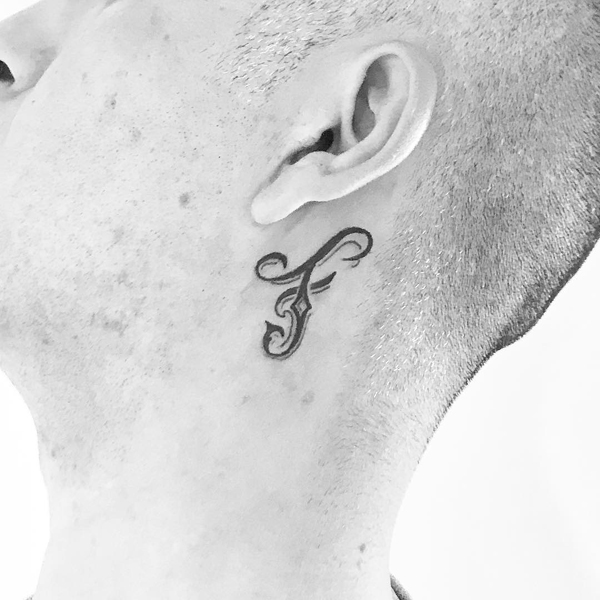 Stilinga F raidės tatuiruotė prie ausies