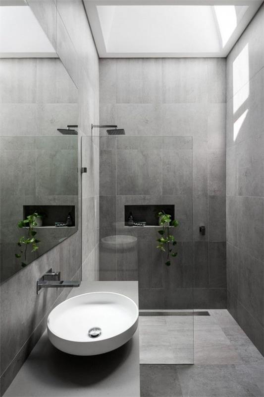 Σχέδια μπάνιου σε γκρι, μεγάλα πλακάκια, λευκό στρογγυλό νιπτήρα, καμπίνα ντους, γυάλινο τοίχο, φως ημέρας από πάνω, πράσινο φυτό μπάνιου