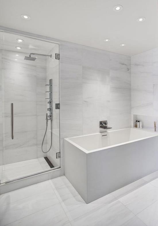 Μπάνιο σε λευκή μπανιέρα ντους γωνιακό γυάλινο τοίχο προβολείς οροφής τεχνητό φως