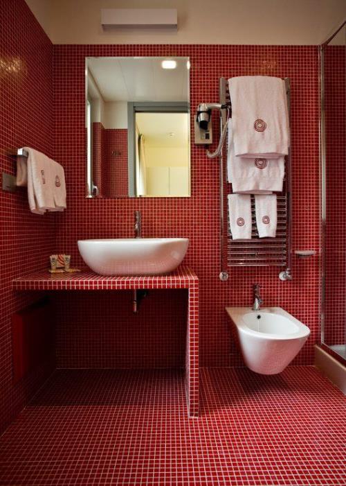 Μπάνιο σε κόκκινους τοίχους ματαιοδοξία δαπέδου με μικρά κόκκινα κεραμίδια καλυμμένα λευκά κονιάματα νεροχύτη τουαλέτας λευκό καθρέφτη τοίχου