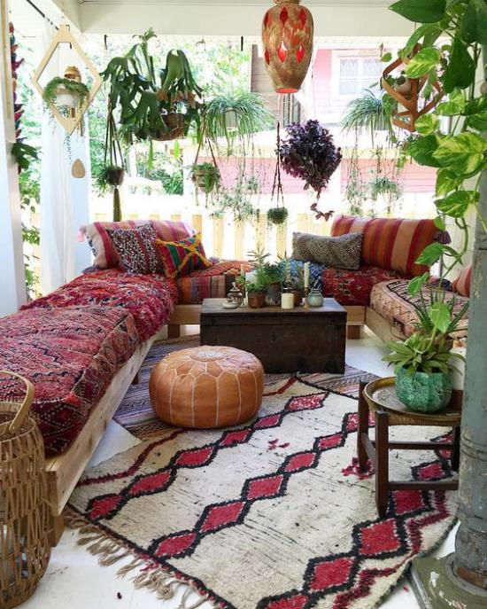 Χαλί βεράντας σε στιλ Boho σε υπόλευκο και μπορντό καναπέ πολύχρωμο κάλυμμα πολλά πράσινα φυτά κρεμαστή λάμπα