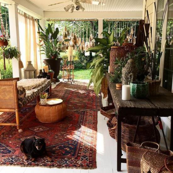 Βεράντα στυλ Boho πολύ κομψό προσκαλώντας περσικό χαλί σε σκούρο κόκκινο πολλά πλούσια πράσινα φυτά ξύλινο σκυλί μπαστούνι