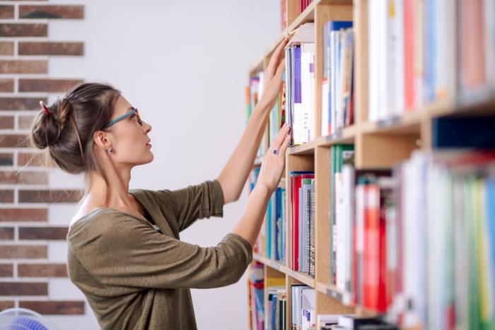 Κρίση Corona στο σπίτι τι να κάνει νεαρή κοπέλα βιβλιοθήκη σπίτι ψάχνει για την τακτοποίηση βιβλίων