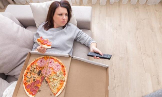 Δίαιτα που πέφτει νεαρή γυναίκα ξαπλωμένη στον καναπέ βλέποντας τηλεόραση τρώει πίτσα κακή συνήθεια