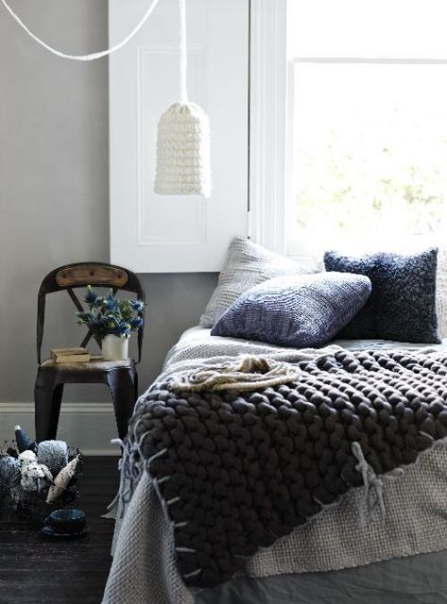 Το άνετο υπνοδωμάτιο το χειμώνα κάνει παχιά πλεκτή κουβέρτα σε γκρι ριχτάρι κρεμαστό φωτιστικό μαξιλαριού