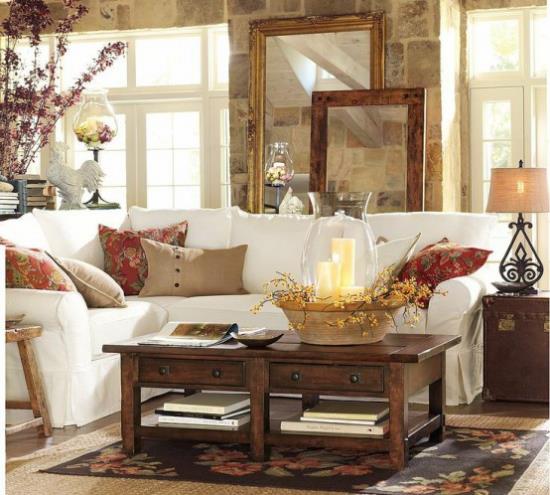 Φθινοπωρινή διακόσμηση στο σαλόνι λευκός γωνιακός καναπές ξύλινο τραπέζι διακοσμημένο με πολύχρωμα μαξιλάρια κεριά κλαδιά σε βάζο άνετο και ζεστό