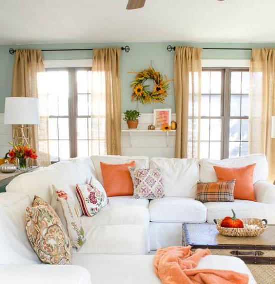 Herbstdeko στο σαλόνι λευκός γωνιακός καναπές πολύχρωμα ριχτά μαξιλάρια ρίξτε κουβέρτα σε πορτοκαλί φθινοπωρινό στεφάνι στον τοίχο