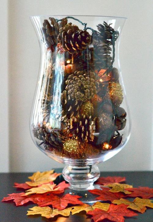 Φθινοπωρινή διακόσμηση με κουκουνάρια ένα ψηλό ποτήρι με χρωματιστούς κώνους διακοσμημένο με χρυσή λάμψη που τραβάει τα βλέμματα