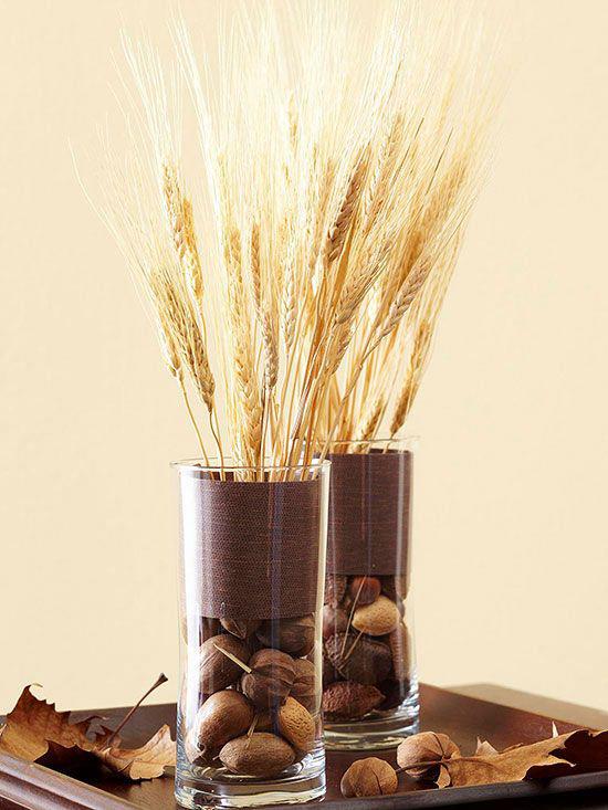 Φθινοπωρινή διακόσμηση με σιτάρι δύο κομψά γυάλινα βάζα μίσχοι σίτου ξηροί καρποί φθινοπωρινά φύλλα σε ξύλινο δίσκο