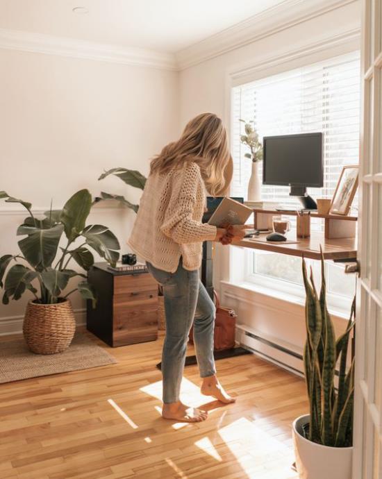 Οδηγός γραφείου στο σπίτι ευχάριστη ατμόσφαιρα χώρου πράσινα φυτά νεαρή γυναίκα που εργάζεται ενώ στέκεται