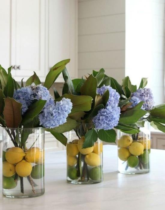 Η άνοιξη της κουζίνας διακοσμεί τις μπλε ορτανσίες σε τρία ποτήρια κίτρινα λεμόνια στο νερό