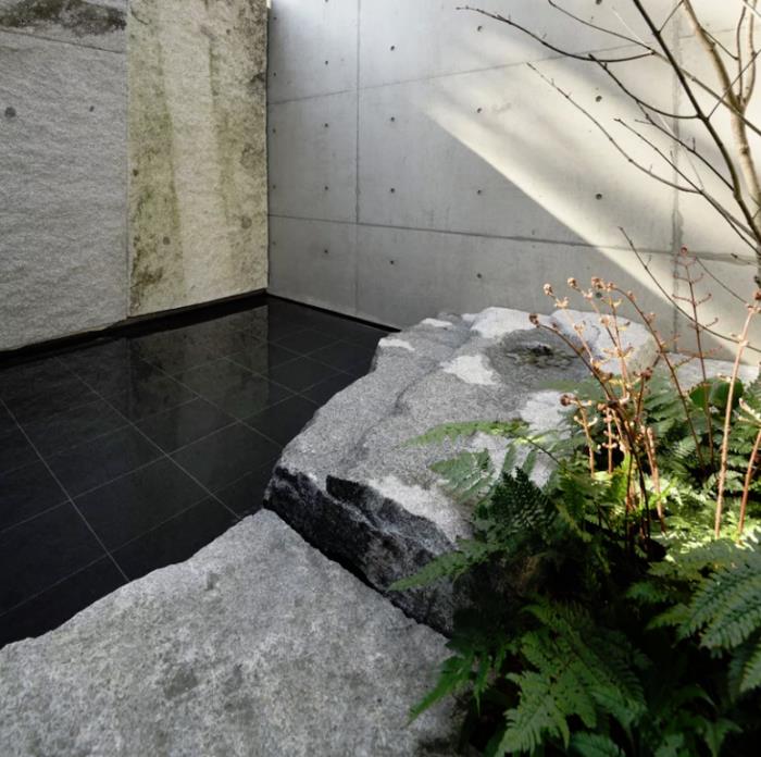 Μινιμαλιστικό πέτρινο και τσιμεντένιο σπίτι στην αυλή της Ιαπωνίας λεία ματ μαύρα πλακάκια φυσική πέτρα μεγάλες πλάκες δέντρο πράσινη φτέρη