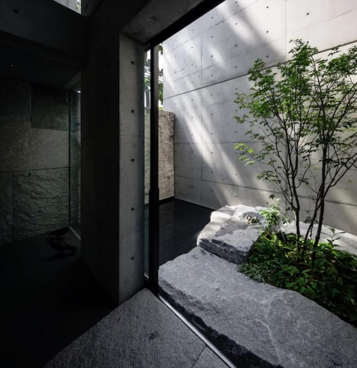 Μινιμαλιστικό πέτρινο και τσιμεντένιο σπίτι στην αυλή της Ιαπωνίας μαύρα πλακάκια από φυσική πέτρα γυάλινες πόρτες φυσικό φως