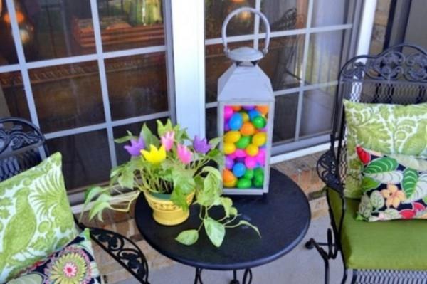 Πασχαλινή διακόσμηση έξω από τη βεράντα διακοσμήστε πολύχρωμα μαξιλάρια καθισμάτων φανάρι με πολύχρωμα αυγά Κατσαρόλα με πράσινο φυτό και λουλούδια σε αυτό