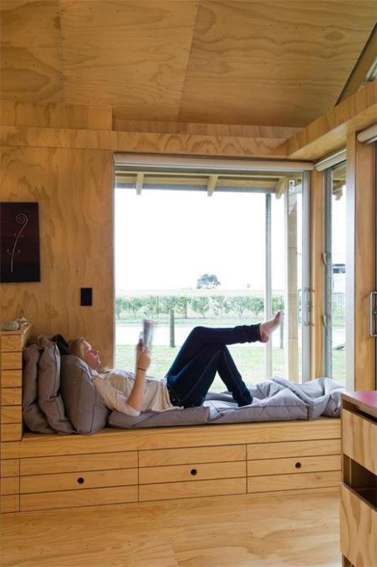 Έξυπνη χρήση του χώρου στο γωνιακό παράθυρο Αγκαλιά γωνιά ανάγνωσης Ταπετσαρισμένος πάγκος Μαξιλάρι Νεαρό κορίτσι που διαβάζει