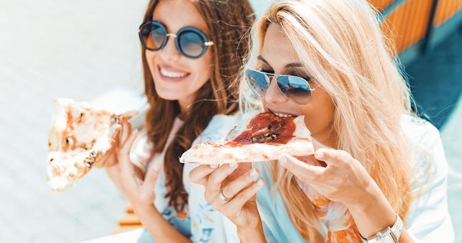 Κανόνας δύο νεαρές γυναίκες που τρώνε πίτσα να χαίρονται να γελούν