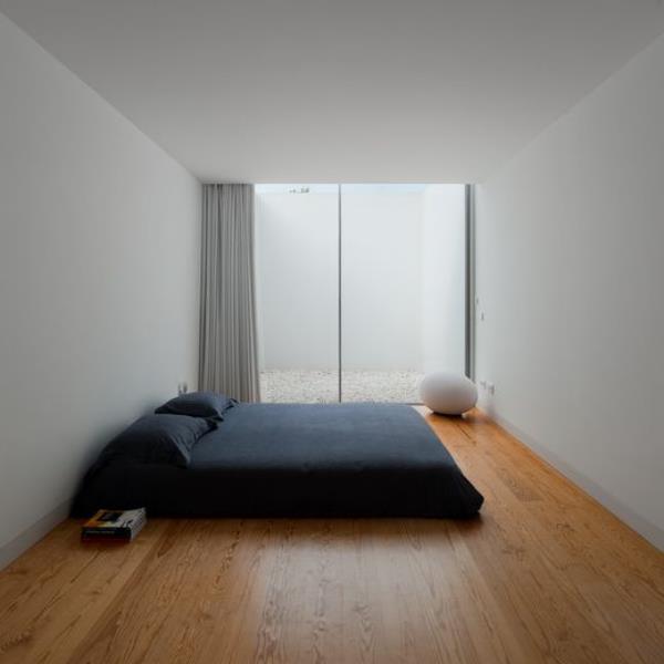 Διακοσμήστε το υπνοδωμάτιο με μινιμαλιστικό τρόπο. Μεγάλο παράθυρο ψηλό στην οροφή. Γκρι τοίχους. Μαύρο κρεβάτι. Δάπεδο από ελαφρύ ξύλο