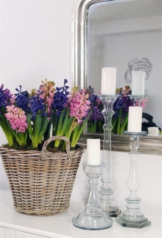 Όμορφοι υάκινθοι διαφορετικών χρωμάτων στο καλάθι μπροστά από έναν καθρέφτη με λευκά κεριά δίπλα του
