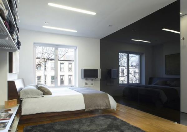 Μαύρος τοίχος σε υψηλή γυαλάδα ως προφορά σε ένα ευρύχωρο λευκό και γκρι υπνοδωμάτιο