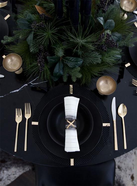 Γιορτάζοντας την παραμονή της Πρωτοχρονιάς στο σπίτι ένα γιορτινό τραπέζι μαύρο τραπεζομάντηλο μαύρο σέρβις χρυσά αστραφτερά μαχαιροπίρουνα λίγο πράσινο στη μέση του τραπεζιού