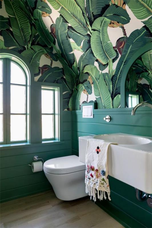 Τροπικό ντεκό στο μπάνιο όμορφη ταπετσαρία μεγάλα φύλλα λευκά έπιπλα μπάνιου πλακάκια δαπέδου τουαλέτα αριστερό παράθυρο