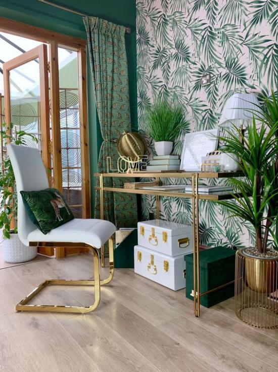 Τροπική διακόσμηση στο γραφείο του σπιτιού μεγάλο φωτεινό δωμάτιο πράσινο χρώμα κυριαρχεί γραφείο πολυθρόνα προφορά ταπετσαρία τοίχου μεγάλα τροπικά φύλλα πράσινα γλάστρες φυτά