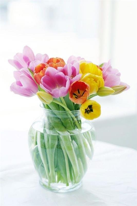 Τουλίπες στο εσωτερικό διαφορετικών χρωμάτων λουλουδιών σε στρογγυλό γυάλινο βάζο