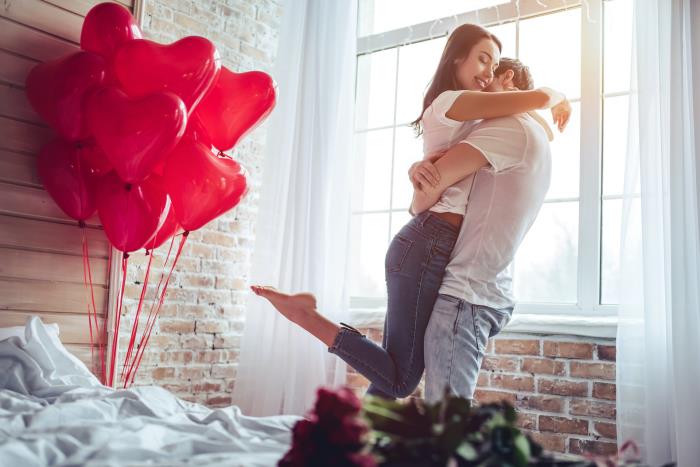 Ερωτευμένος το ζώδιό του για την ημέρα του Αγίου Βαλεντίνου κόκκινα μπαλόνια κόκκινα τριαντάφυλλα ευτυχισμένο το νεαρό ζευγάρι του στην κρεβατοκάμαρα