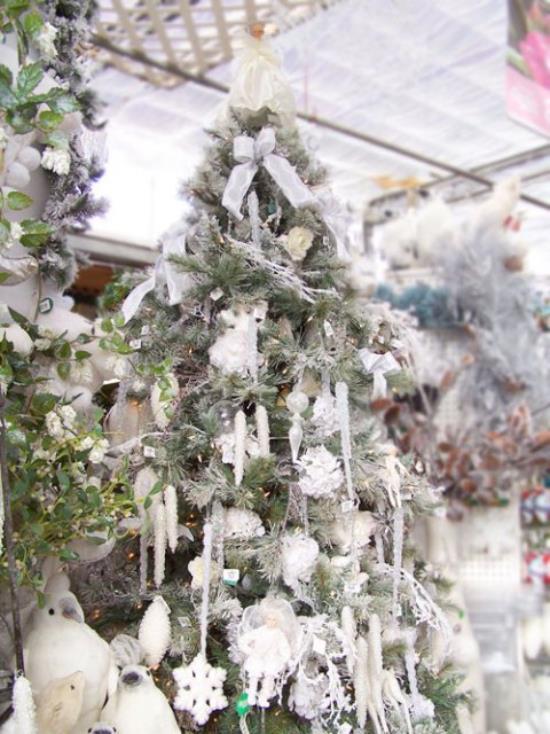 Χριστουγεννιάτικο δέντρο στολίζει σε λευκό και ασημένιο ψηλό χριστουγεννιάτικο δέντρο λευκές γιρλάντες κώνοι αστέρια μπάλες τόξα