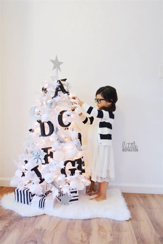 Χριστουγεννιάτικο δέντρο στολίζει σε λευκό και ασημένιο μικρό δέντρο σε λευκή διακόσμηση σε μαύρη αντίθεση μεγάλα γράμματα κοριτσάκι