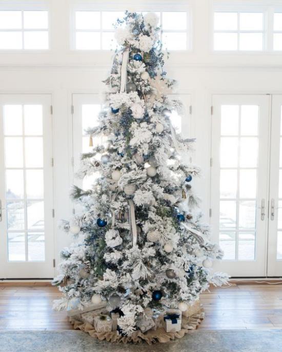 Διακοσμήστε το χριστουγεννιάτικο δέντρο σε λευκό και ασημί χρώμα μπροστά από το παράθυρο, τοποθετήστε μερικές λαμπερές μπλε μπάλες ως τόνους