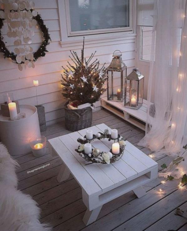 Χριστουγεννιάτικη διακόσμηση για το μπαλκόνι όλα σε λευκό πολυάριθμα φώτα και κεριά Advent στεφάνι σε χαμηλό λευκό τραπέζι στη μέση
