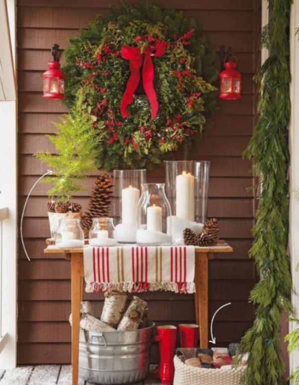 Χριστουγεννιάτικη διακόσμηση για το μπαλκόνι με πολύ πράσινο έλατο, κόκκινα τόξα, κόκκινες μπότες, λευκά κεριά, ζεστή και ελκυστική