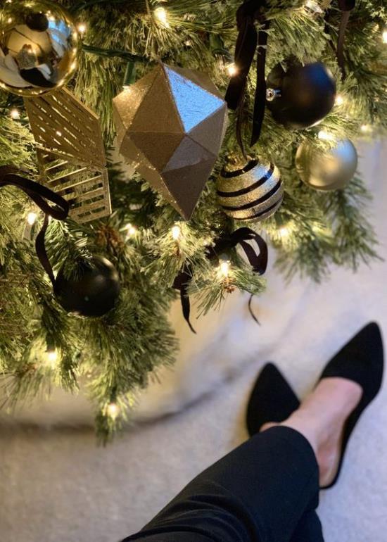 Χριστουγεννιάτικη διακόσμηση σε χρυσό και μαύρο χριστουγεννιάτικο δέντρο χρυσές κίτρινες και μαύρες μπάλες επιπλέον στολίδια μια γυναίκα δίπλα