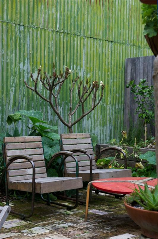 ένα εκλεκτικό σπίτι από πράσινους λαμαρίνες τοίχους, άθλιες καρέκλες κήπου και ένα κόκκινο τραπεζάκι