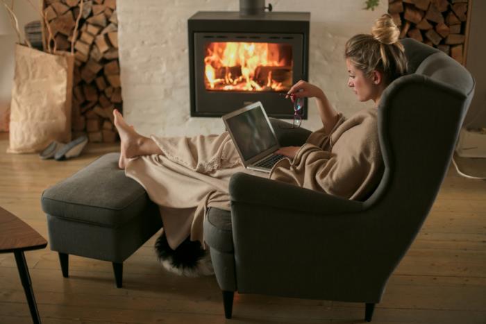 υγιής και χαρούμενος το χειμώνα νεαρή γυναίκα στην πολυθρόνα μπροστά από το τζάκι που καίει ένα βιβλίο στο χέρι της καυσόξυλα ζεστή ζεστή ατμόσφαιρα δωματίου