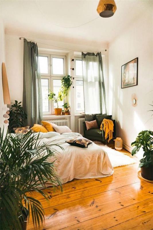 μικρό υπνοδωμάτιο ξύλινο πάτωμα πολλά πράσινα φυτά κρεβάτια στρωμένα με πράσινη πολυθρόνα στη γωνία δίπλα στα παράθυρα με τόνους με κίτρινο χρώμα