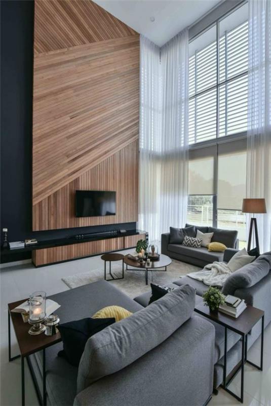 μοντέρνο σαλόνι σε ξύλινο τοίχο σε δύο επίπεδα, καθώς τα γκρίζα έπιπλα μαξιλαριών ματιών τραπέζια κεριά φαίνονται φιλόξενα και ζεστά