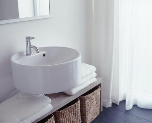 λευκό χρώμα νεροχύτη μπάνιου γύρω από ψάθινες πετσέτες καλαθιού