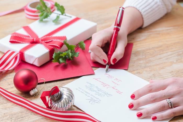 νεαρή γυναίκα που γράφει χριστουγεννιάτικες κάρτες με κόκκινα νύχια, κόκκινο στυλό και διακοσμήσεις διακοπών