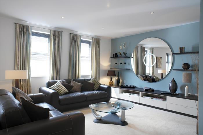 σχεδιασμός σαλονιού μπλε τοίχου με έμφαση σε στρογγυλό τοίχο καθρέφτη μαύρους δερμάτινους καναπέδες